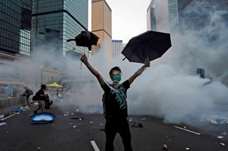 Um manifestante ergue o chapéu-de-chuva no momento em que a polícia anti-motim tenta dispersar as pessoas que bloqueiam as ruas em frente à sede do Governo de Hong Kong Um manifestante ergue o chapéu-de-chuva no momento em que a polícia anti-motim tenta dispersar as pessoas que bloqueiam as ruas em frente à sede do Governo de Hong Kong