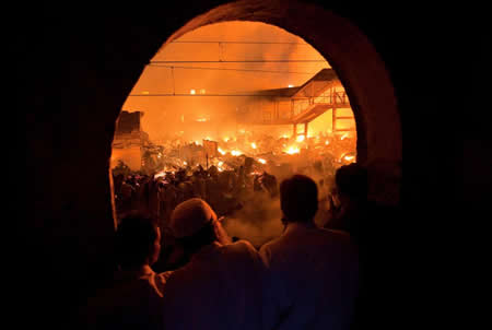 Um grupo de pessoas assiste a partir de um interior de um prédio a um incêndio numa favela em Mumbai, na Índia. Créditos: Reuters / Vivek Prakash Um grupo de pessoas assiste a partir de um interior de um prédio a um incêndio numa favela em Mumbai, na Índia. Créditos: Reuters / Vivek Prakash