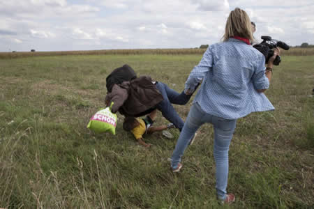 Um migrante que carrega uma criança cai após tropeçar na operadora de câmara de TV, Petra Laszlo, enquanto tenta escapar de um ponto de coleta na vila de Roszke, na Hungria. Créditos: Reuters / Marko Djurica Um migrante que carrega uma criança cai após tropeçar na operadora de câmara de TV, Petra Laszlo, enquanto tenta escapar de um ponto de coleta na vila de Roszke, na Hungria. Créditos: Reuters / Marko Djurica