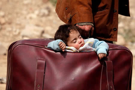 Uma criança dorme dentro de uma mala de mão enquanto é transportada em Ghouta, Síria.  Uma criança dorme dentro de uma mala de mão enquanto é transportada em Ghouta, Síria.