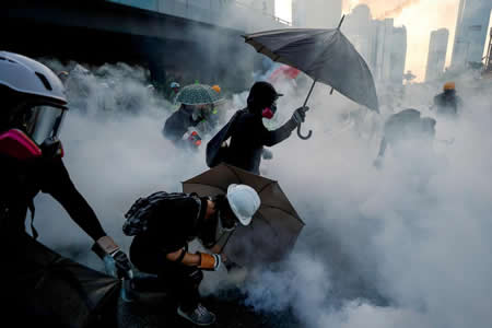 Manifestantes em protesto contra o governo protegem-se com chapéus-de-chuva contra o gás lacrimogéneo lançado pela polícia em Hong Kong. Manifestantes em protesto contra o governo protegem-se com chapéus-de-chuva contra o gás lacrimogéneo lançado pela polícia em Hong Kong.