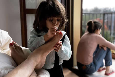 O professor Marzio Toniolo, 35 anos, tira uma foto da sua filha Bianca, de dois anos, a pintar-lhe as unhas dos pés, enquanto a sua mulher, mãe da Bianca, Chiara Zuddas, olha pela varanda de casa durante o surto de coronavírus, em San Fiorano, Itália