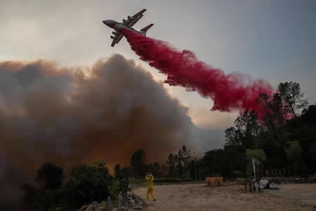 Uma mulher fotografa um avião de combate de incêndios a despejar retardante em Deer Park, Califórnia. 