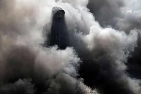 Um manifestante iraquiano caminha entre o fumo de pneus a arder durante protestos contra o governo em Kerbala, Iraque. 